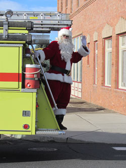 Santa waves from back of fire truck in front of Harrington Opera House